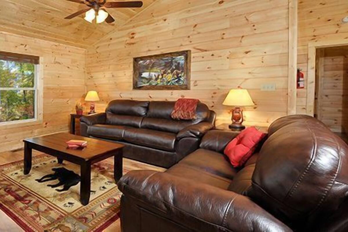 Interior acogedor de una cabaña de troncos con chimenea, sofá de cuero y televisor.