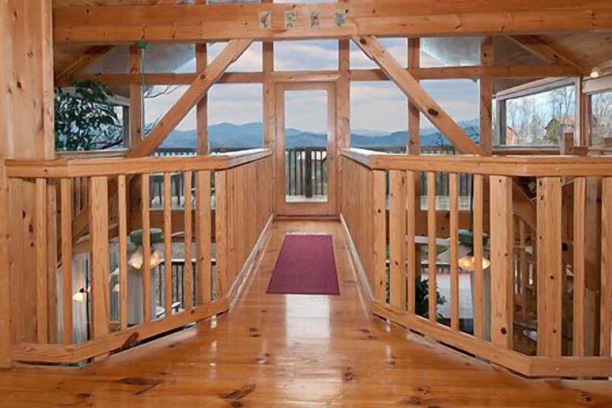 Una cabaña de madera con un pasillo central que lleva a un balcón con vistas a las montañas.
