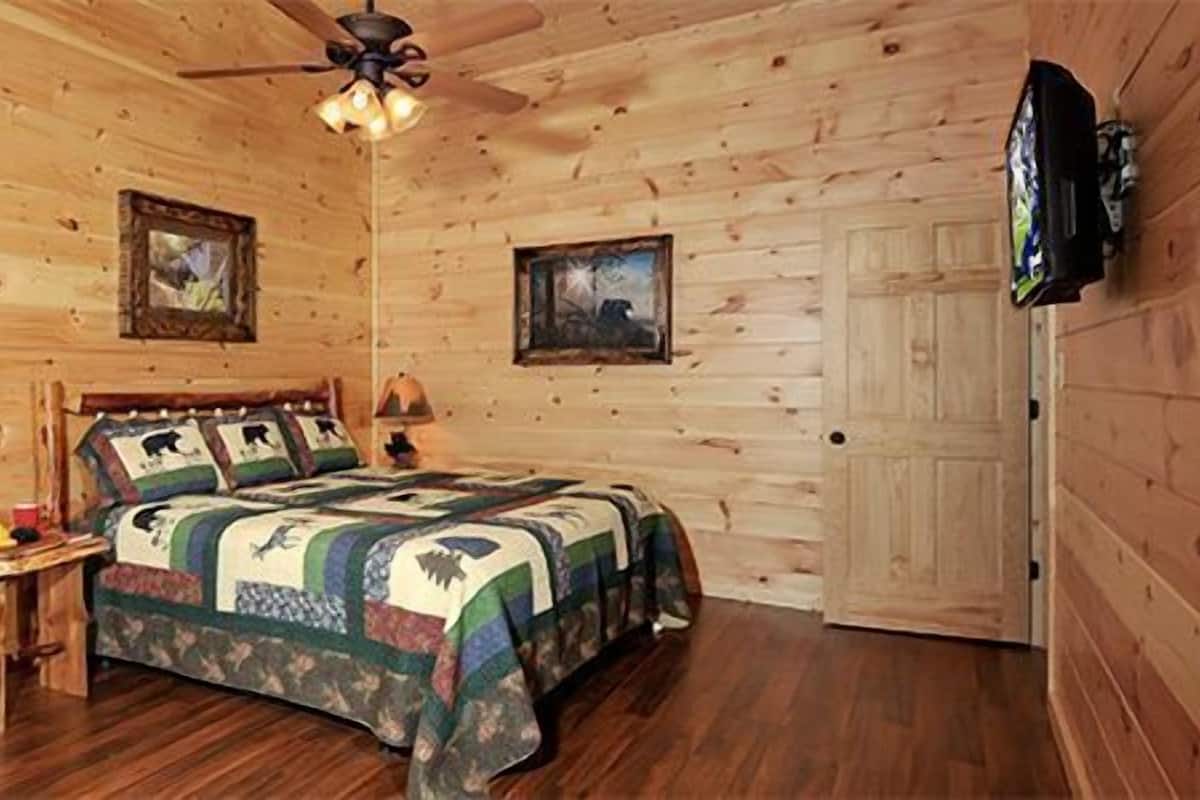 Un dormitorio de cabaña de madera con una cama, un ventilador de techo y dos cuadros en las paredes.