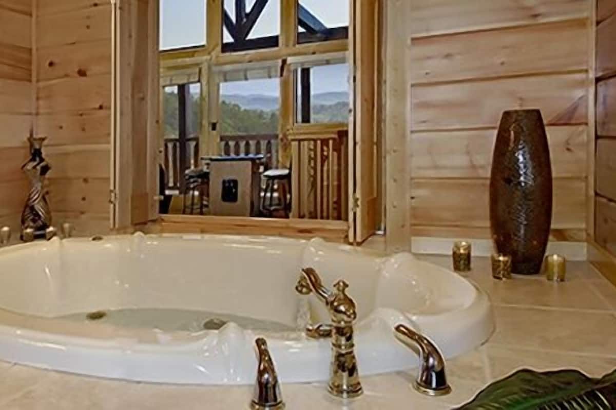 Un baño de cabaña de madera con una bañera grande, un lavamanos y un ventanal con vistas a una terraza.