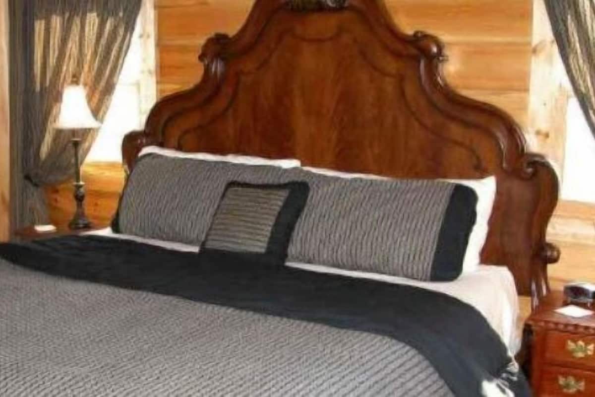 Una cama de madera con cabecera, una colcha gris y dos almohadas.