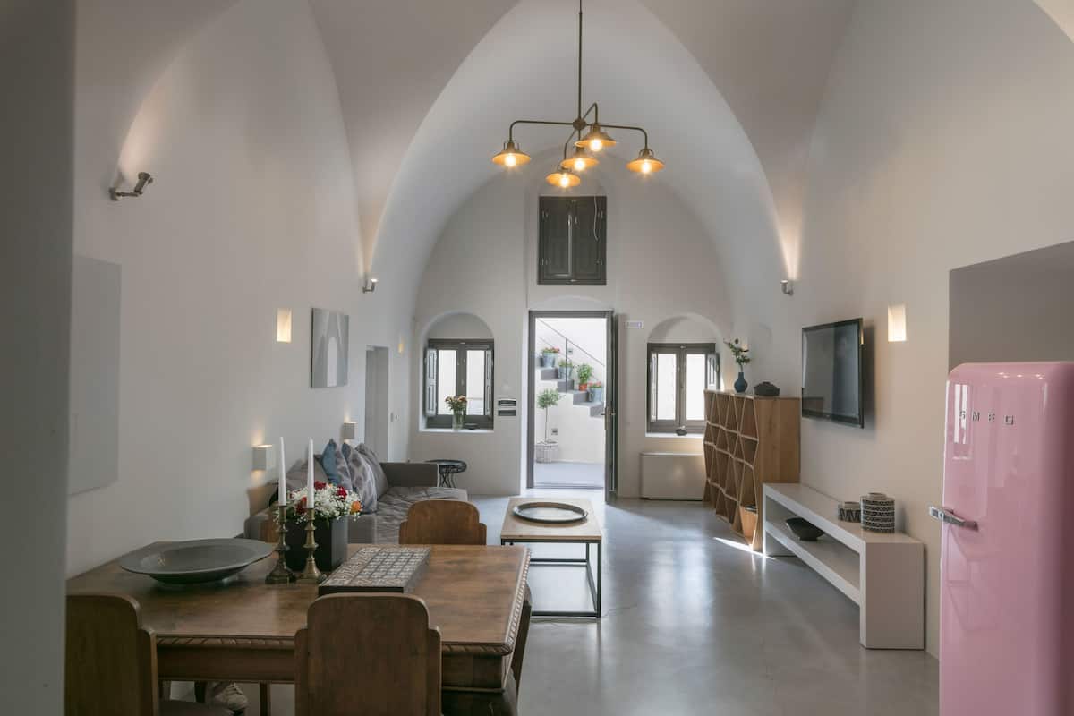 A modern kitchen with a dining area, featuring a pink refrigerator, wooden furniture, and a high arched ceiling.