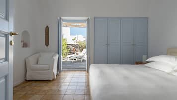 A bedroom with a bed, a white chair, a wardrobe, and a view of the outside.