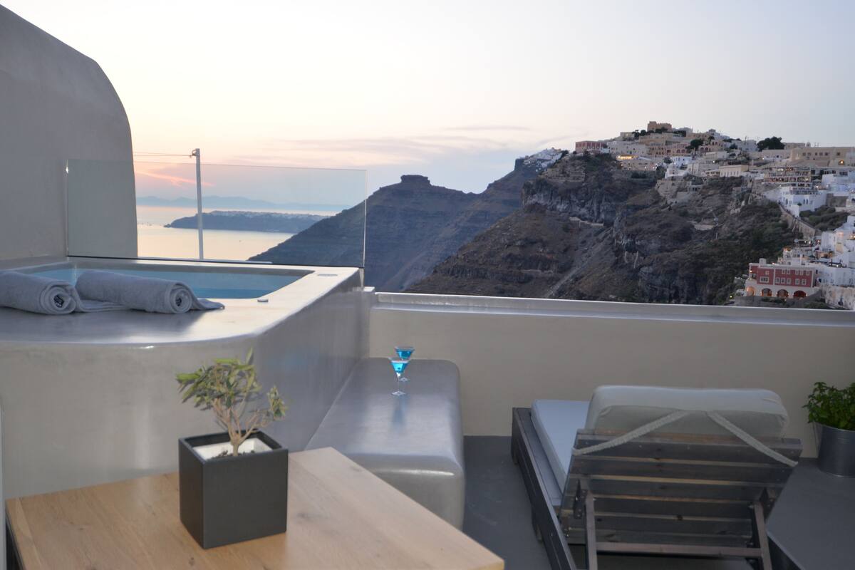 A balcony with a view of a coastal town, a small pool, and a table with a plant.