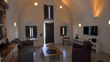 A spacious living room with a high ceiling, a flat-screen TV mounted on the wall, and a comfortable seating area with a sofa and a chair.