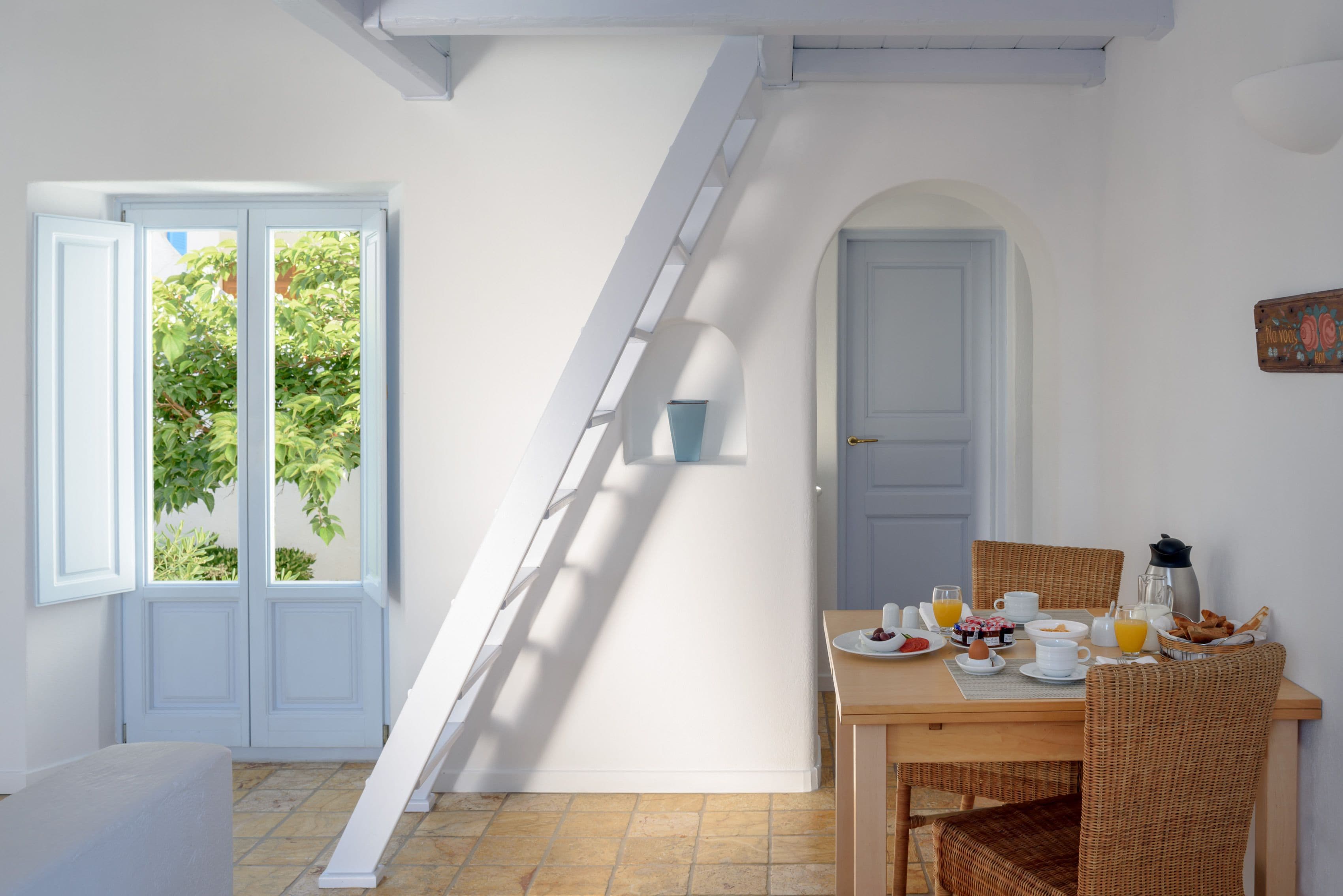 A dining area with a table set for breakfast, a staircase, and a door leading outside.