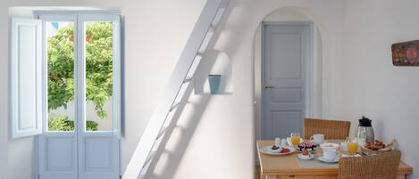 Un comedor con una mesa dispuesta para el desayuno, una escalera y una puerta que da al exterior.