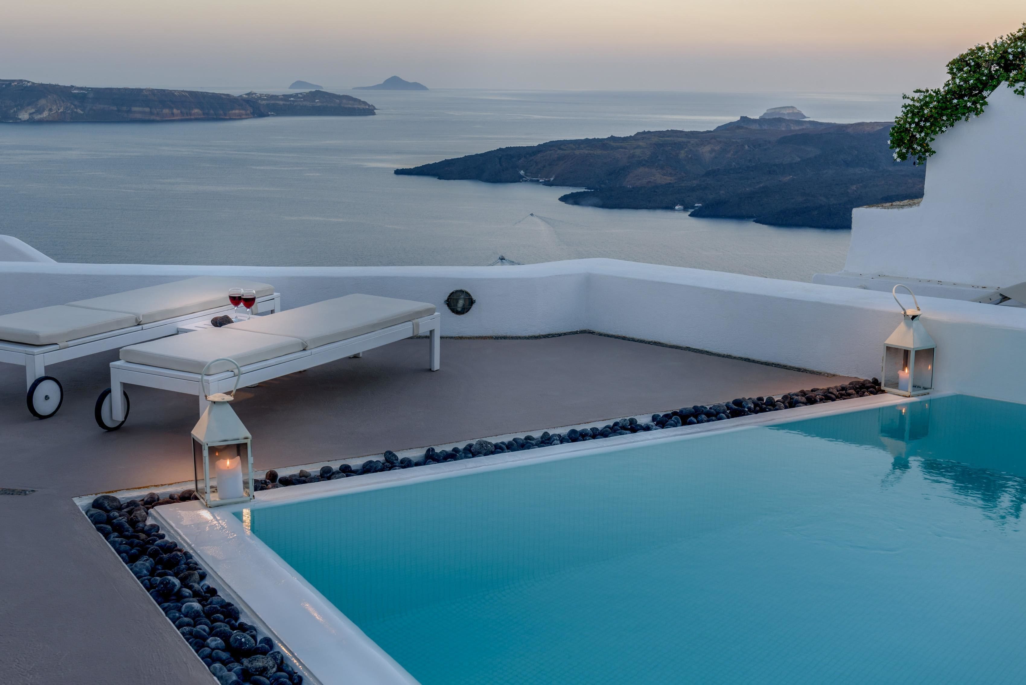 A poolside area with a view of the sea, lounge chairs, and a candle-lit lantern.