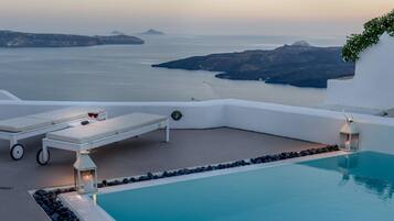 A poolside area with a view of the sea, lounge chairs, and a candle-lit lantern.