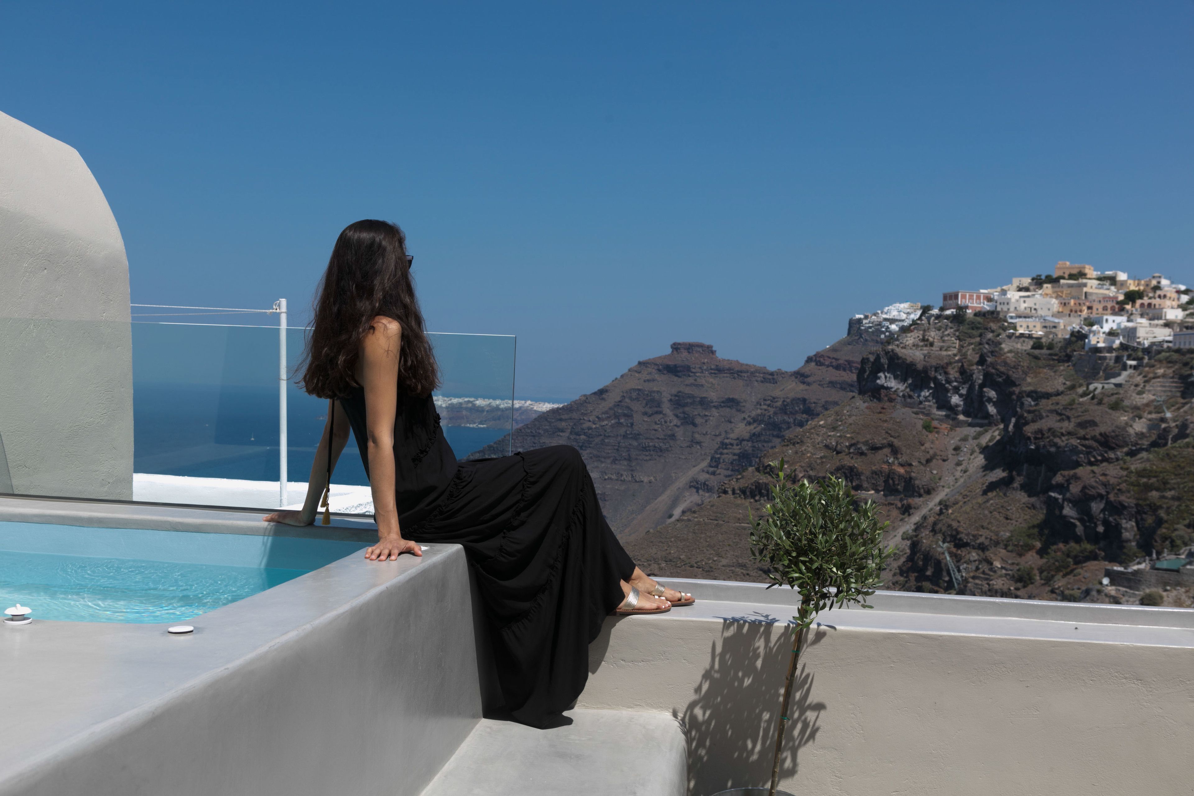 A woman sitting by a pool with a view of a hillside town.