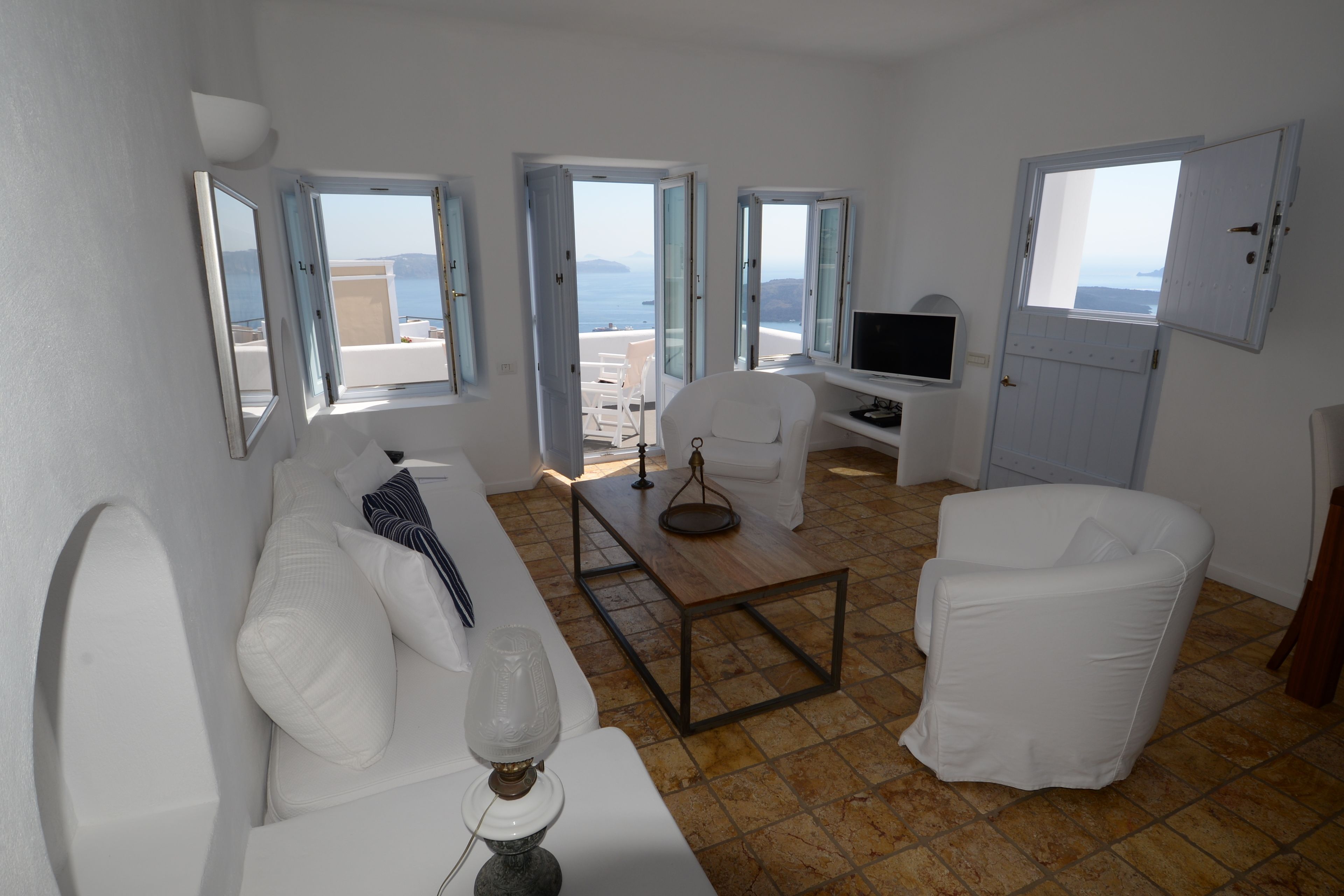 A bright living room with white furniture, large windows, and a view of the sea.