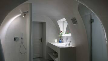 Un baño moderno con techo curvo, una ducha, un lavabo con espejo y un florero con flores.