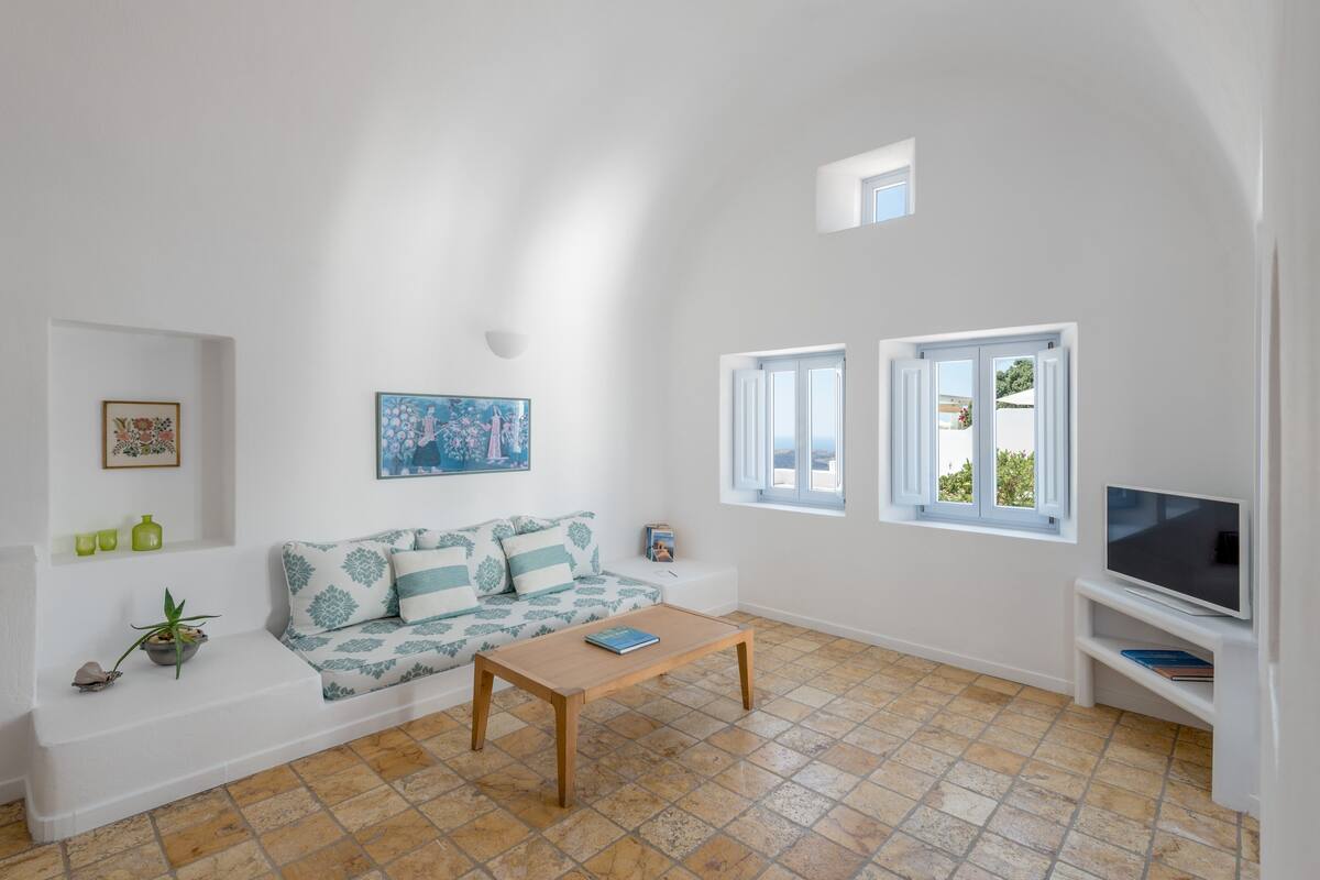 A living room with a sofa, a coffee table, a TV, and two windows.