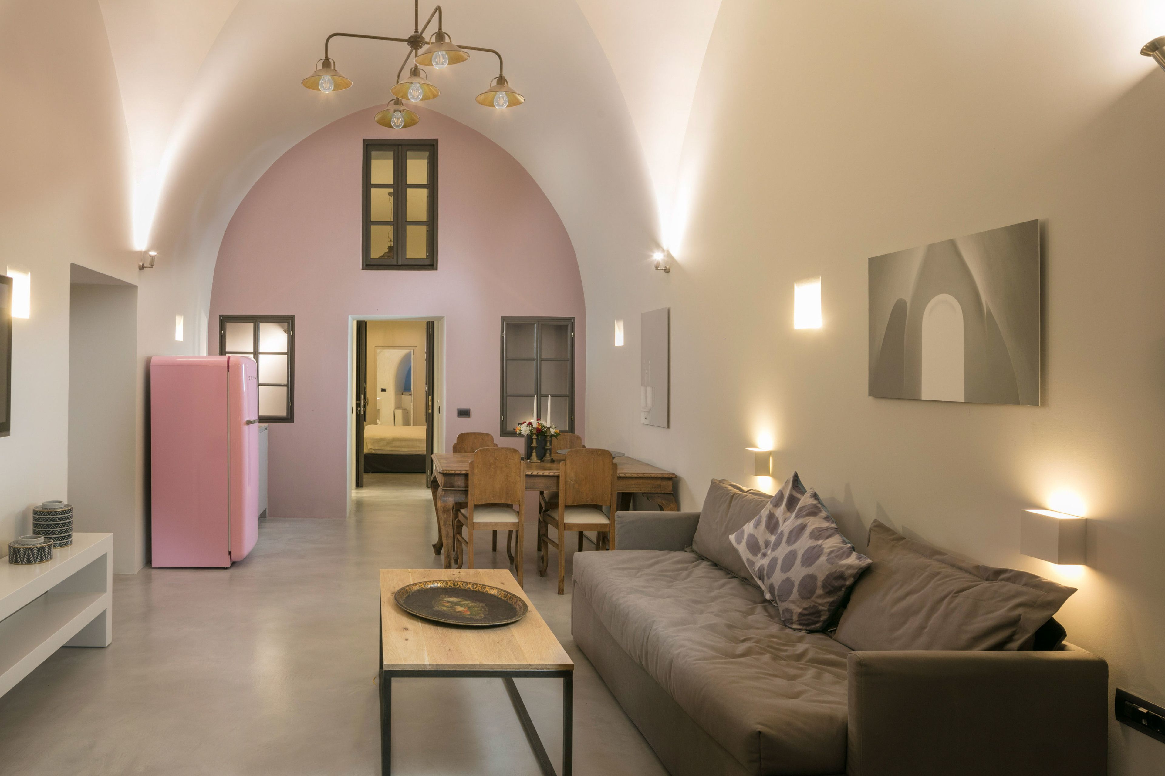 Un soggiorno spazioso con un frigorifero rosa, un tavolino in legno e un divano beige. Si vede anche una zona pranzo con tavolo e sedie, e una cucina sullo sfondo.