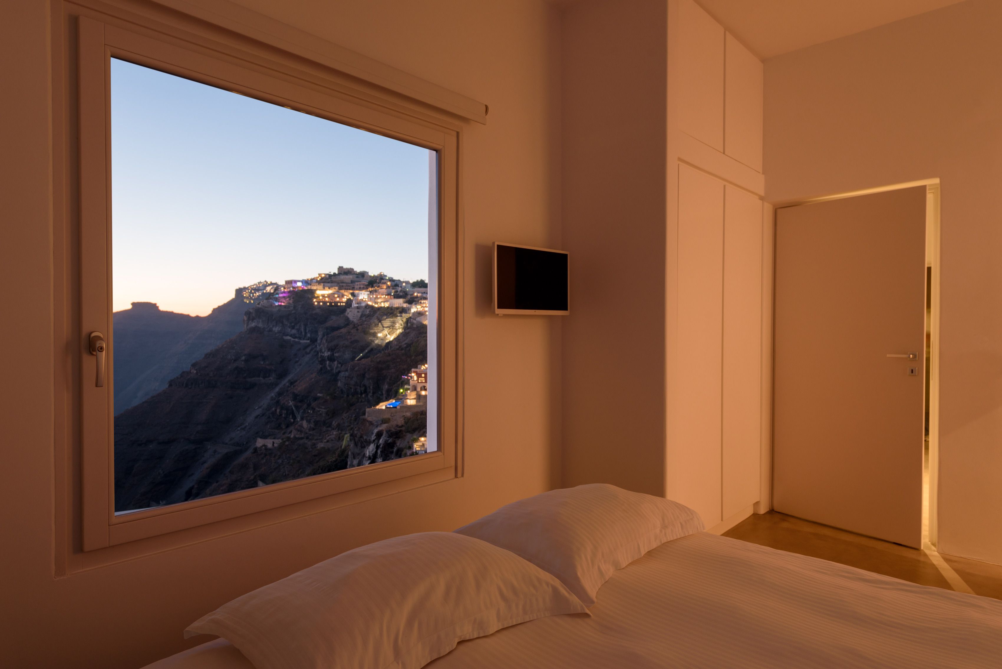 A bedroom with a large window overlooking a mountainous landscape at dusk.