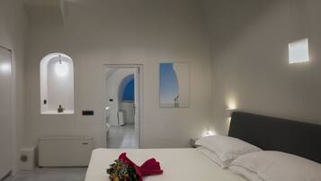 A modern hotel room with a large bed, a bedside table, a small bedside lamp, a wall-mounted mirror, and a door leading to another room.