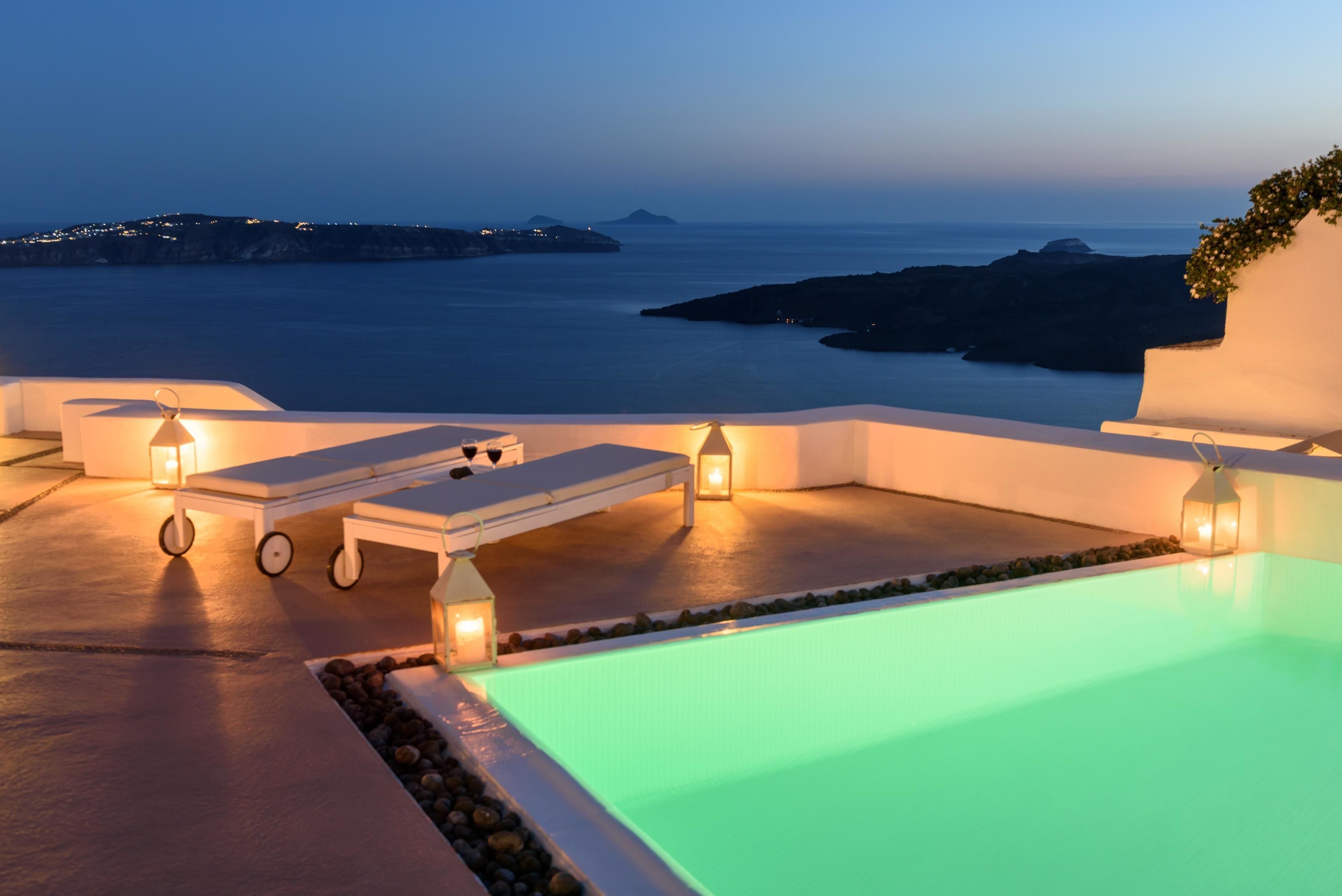 Piscina infinita con vista al mar, sillas de descanso e iluminación ambiental.