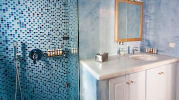 A bathroom with a tiled shower wall, a sink with a mirror, and cabinets.