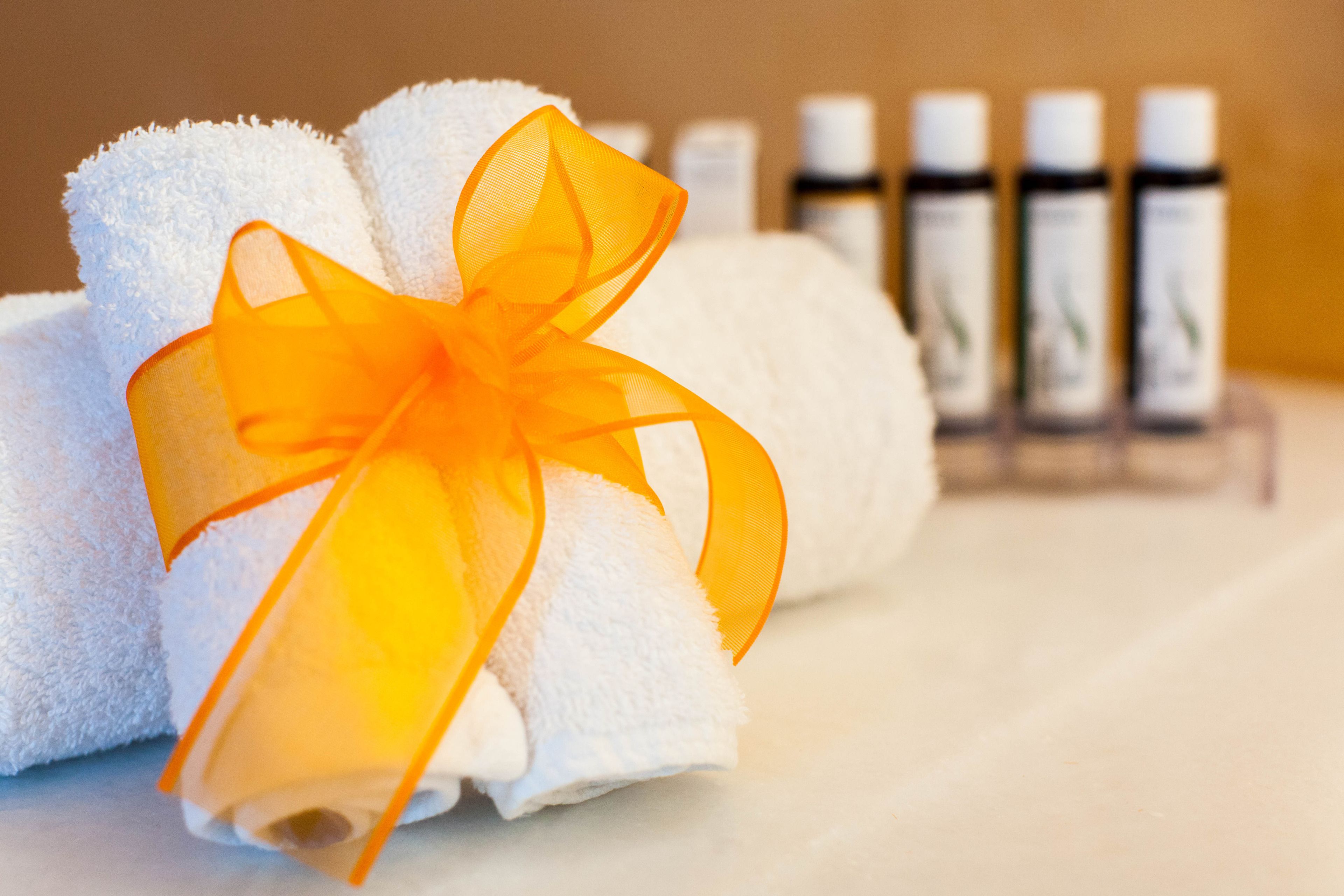 A neatly rolled white towel with an orange ribbon tied around it, placed in front of a row of white bottles, likely containing toiletries.