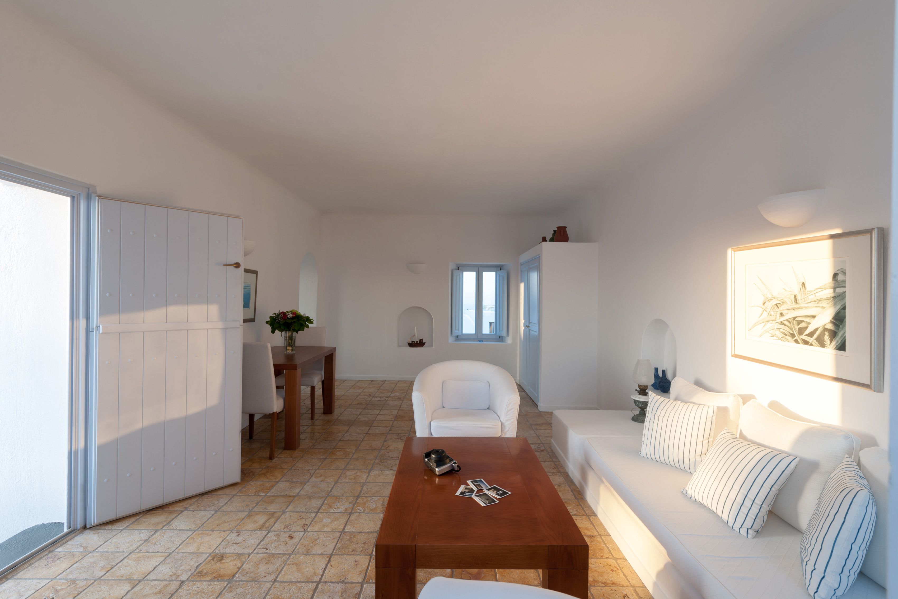 A modern living room with a white sofa, a wooden coffee table, and a dining area with a white chair and table.