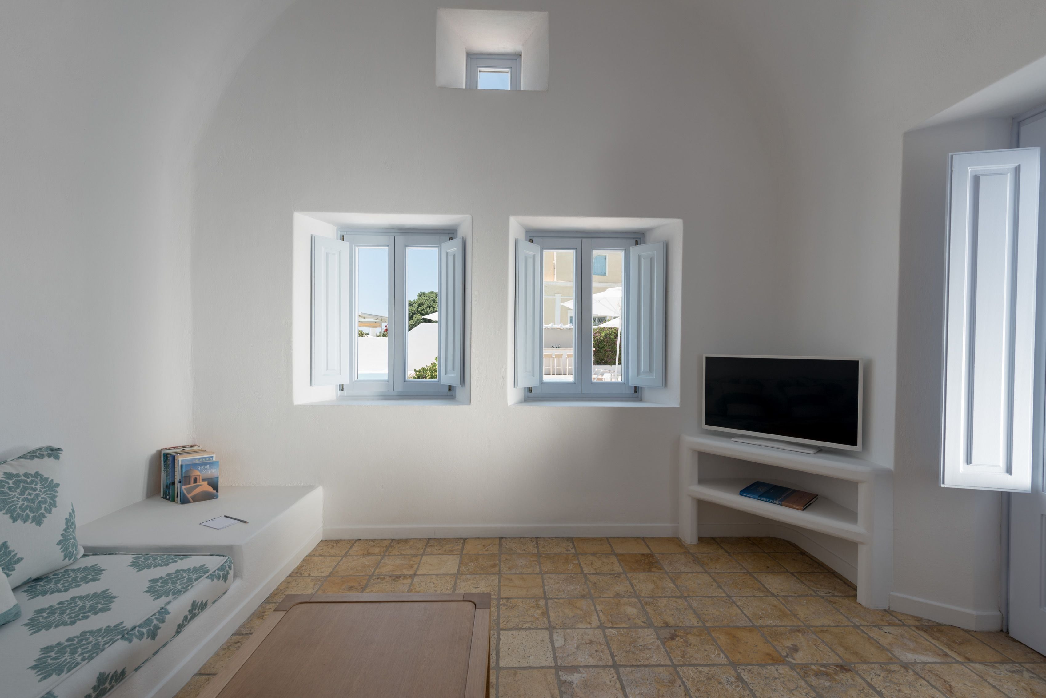 A living room with a sofa, a TV on a stand, two windows, and a small skylight.