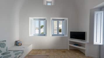 A living room with a sofa, a TV on a stand, two windows, and a small skylight.