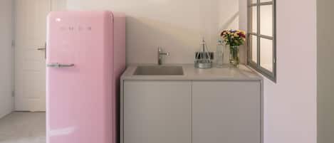 A compact kitchen with a pink refrigerator, a sink, and a window with a view.