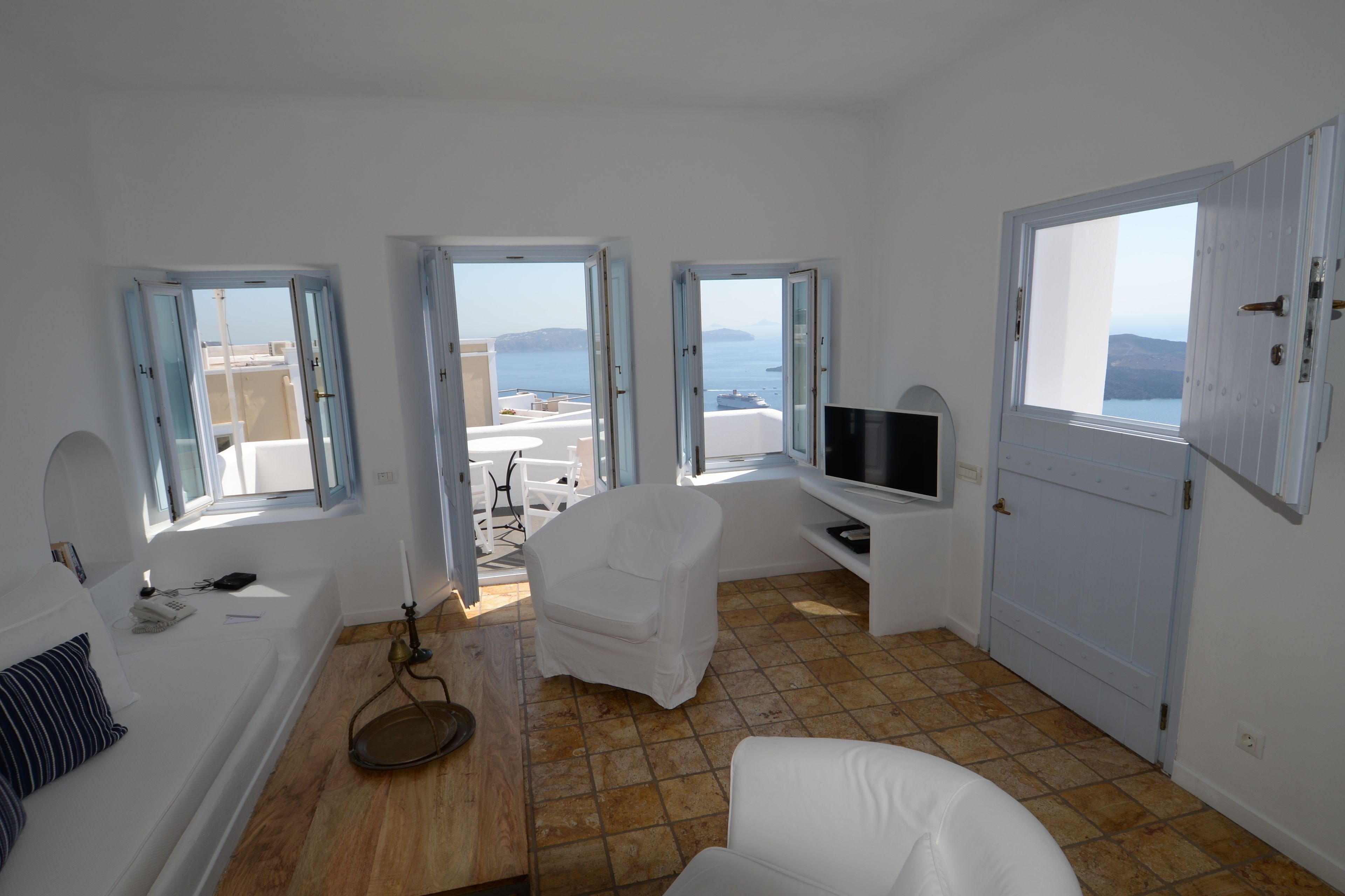 Una habitación con un sofá blanco, un mueble para la televisi ón y vista al mar a través de puertas abiertas.