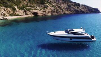 A yacht on clear blue water with a rocky coastline in the background.