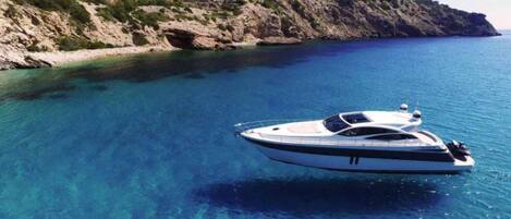 A yacht on clear blue water with a rocky coastline in the background.