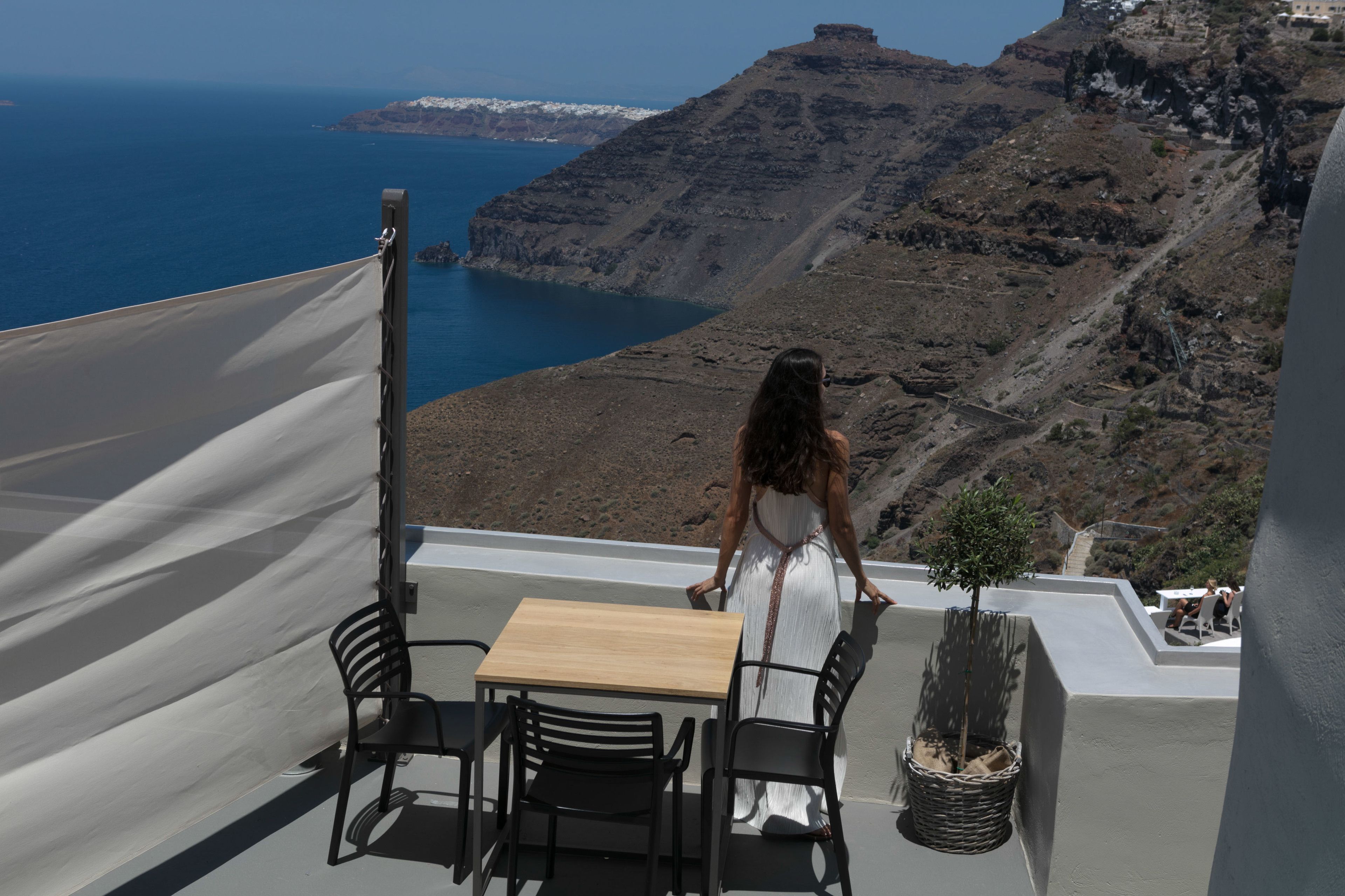Une terrasse avec une table et des chaises, offrant une vue sur un paysage côtier avec des falaises et la mer.