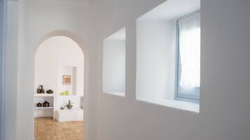 Un pasillo estrecho con un arco blanco que da a una habitación con ventana y estantes con diversos objetos.