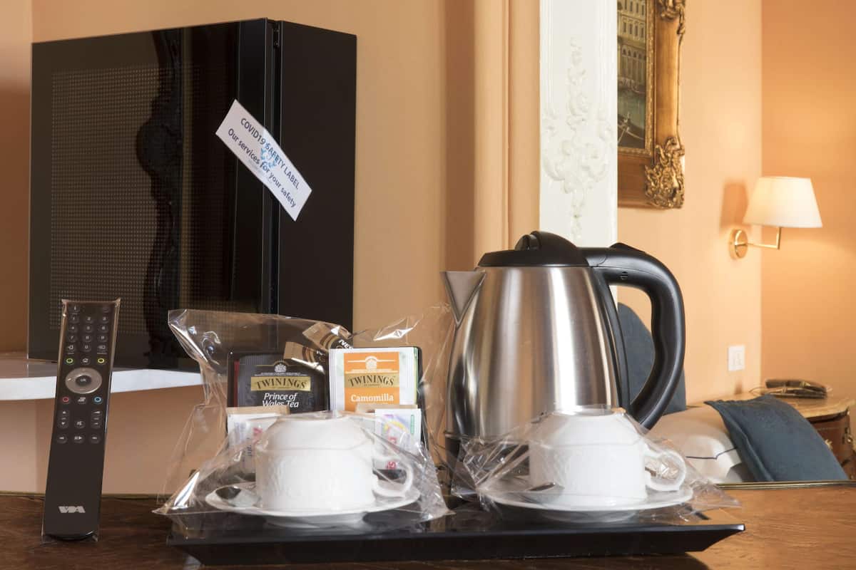 A hotel room with a TV, remote control, a tray with cups and a kettle, and a sign indicating COVID-19 safety measures.
