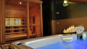 Une salle de spa dotée d’un sauna en bois, d’un bain à remous avec des bougies et d’un luminaire fixé au mur.