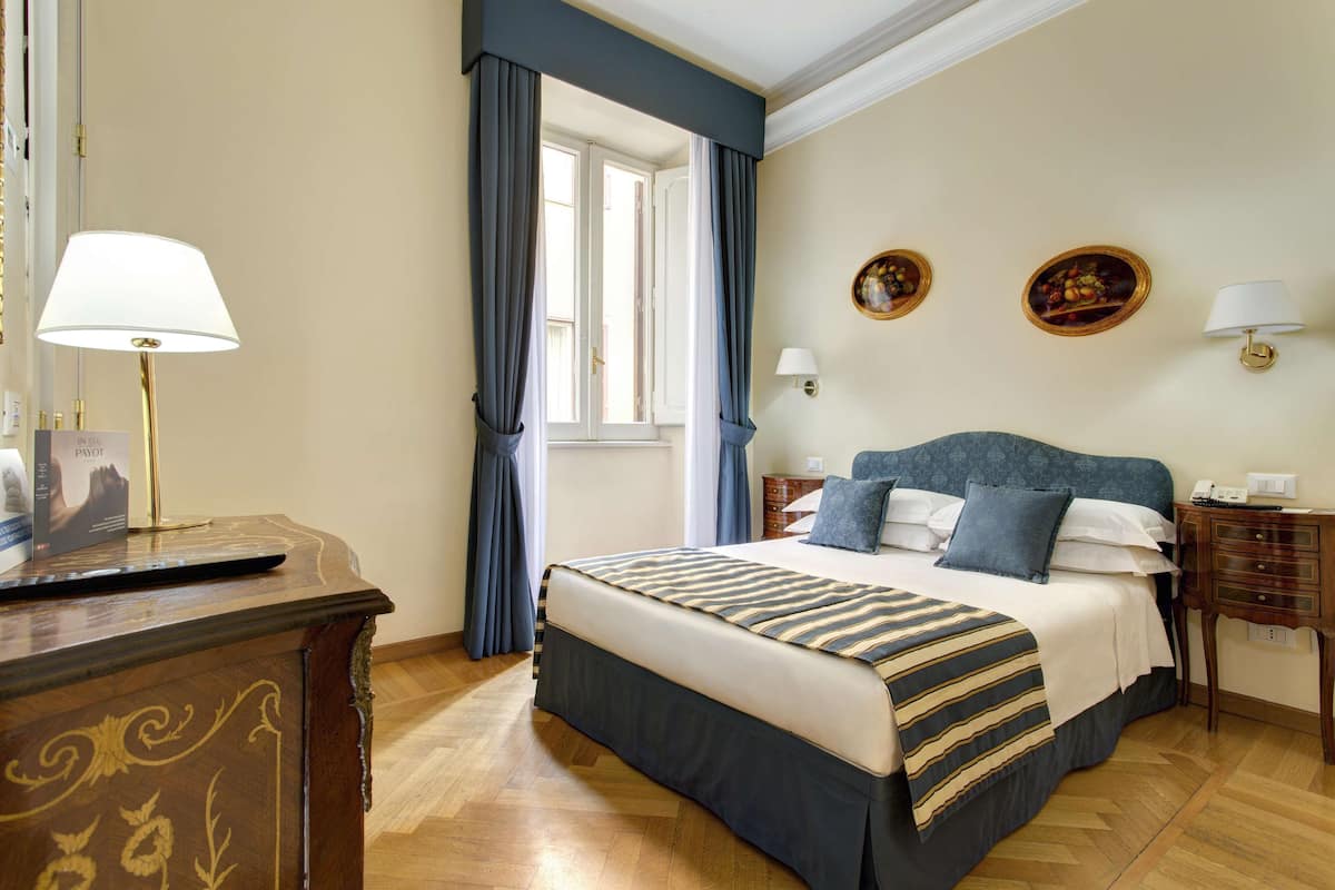 A hotel room with a bed, bedside tables, a desk, and curtains.