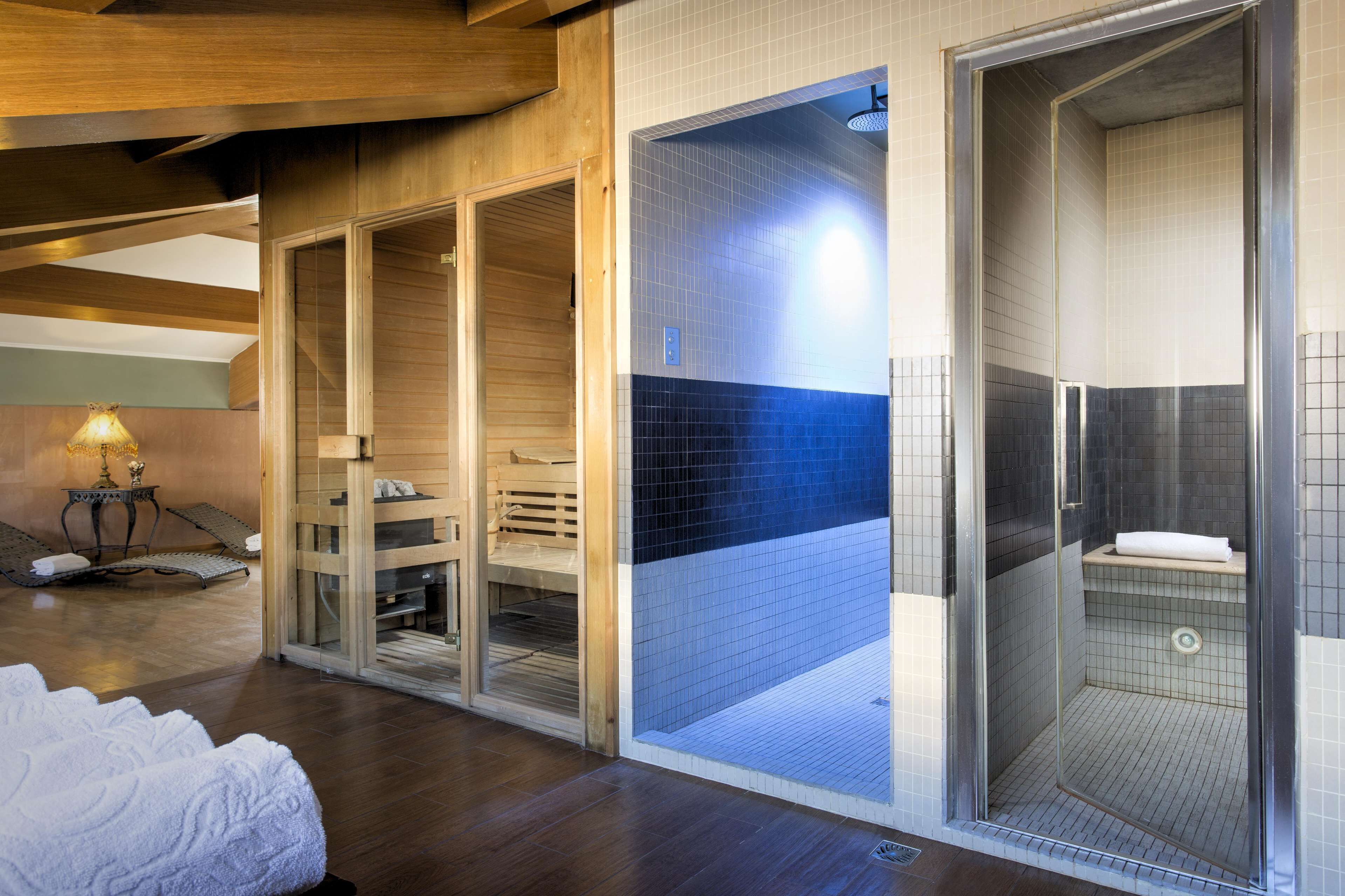 A spa area with a wooden bench, a glass-enclosed shower, and a tiled wall.