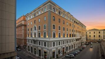 A multi-story hotel with a classic architectural style, featuring a central courtyard and a row of shops on the ground floor.