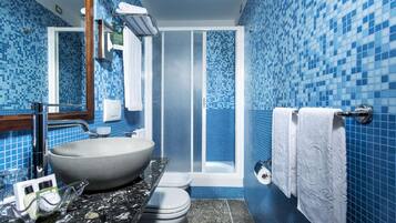 A bathroom with a large vessel sink, a toilet, a shower enclosure, and blue mosaic tiles.