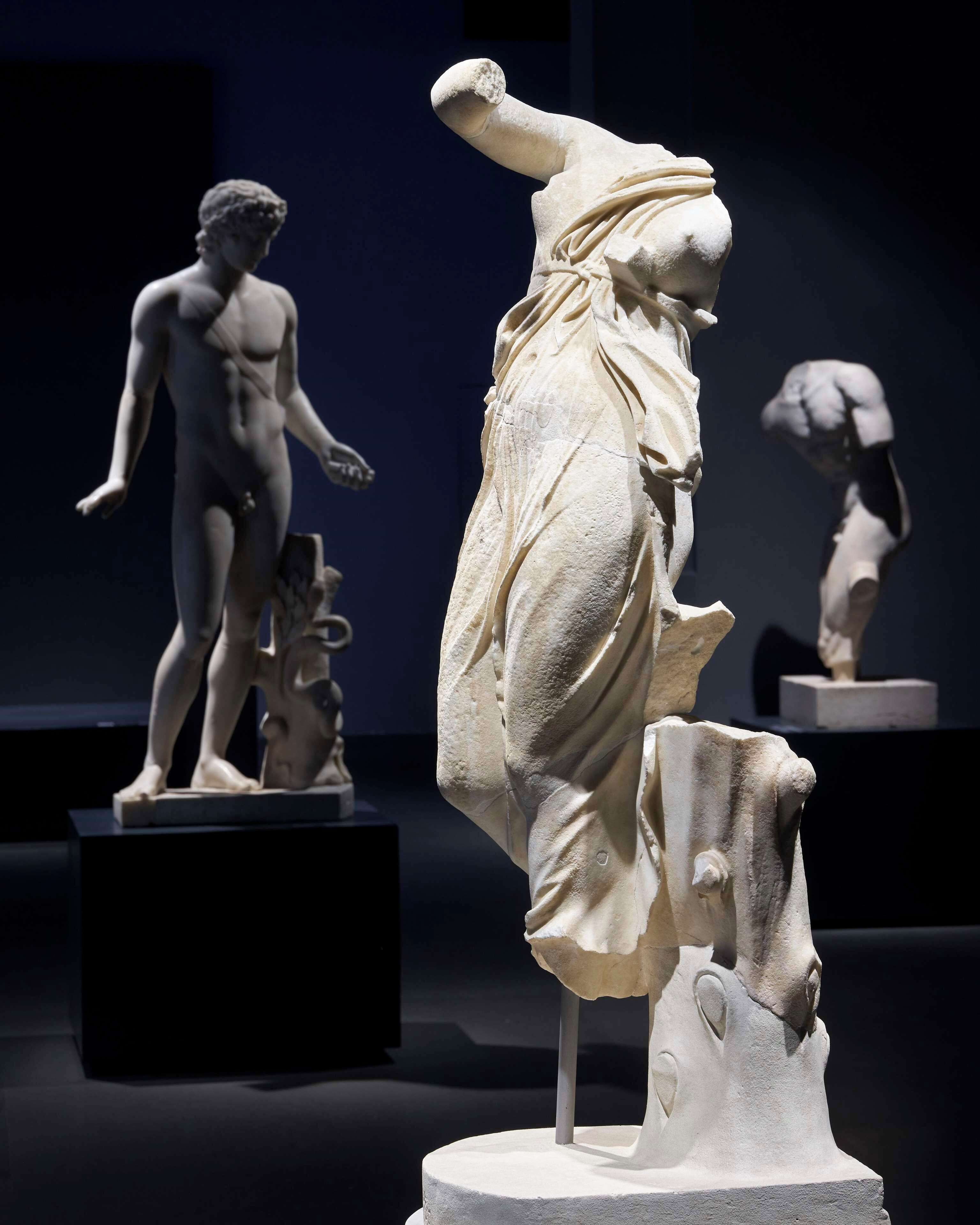 Una escultura clásica en un museo, con otras esculturas al fondo.