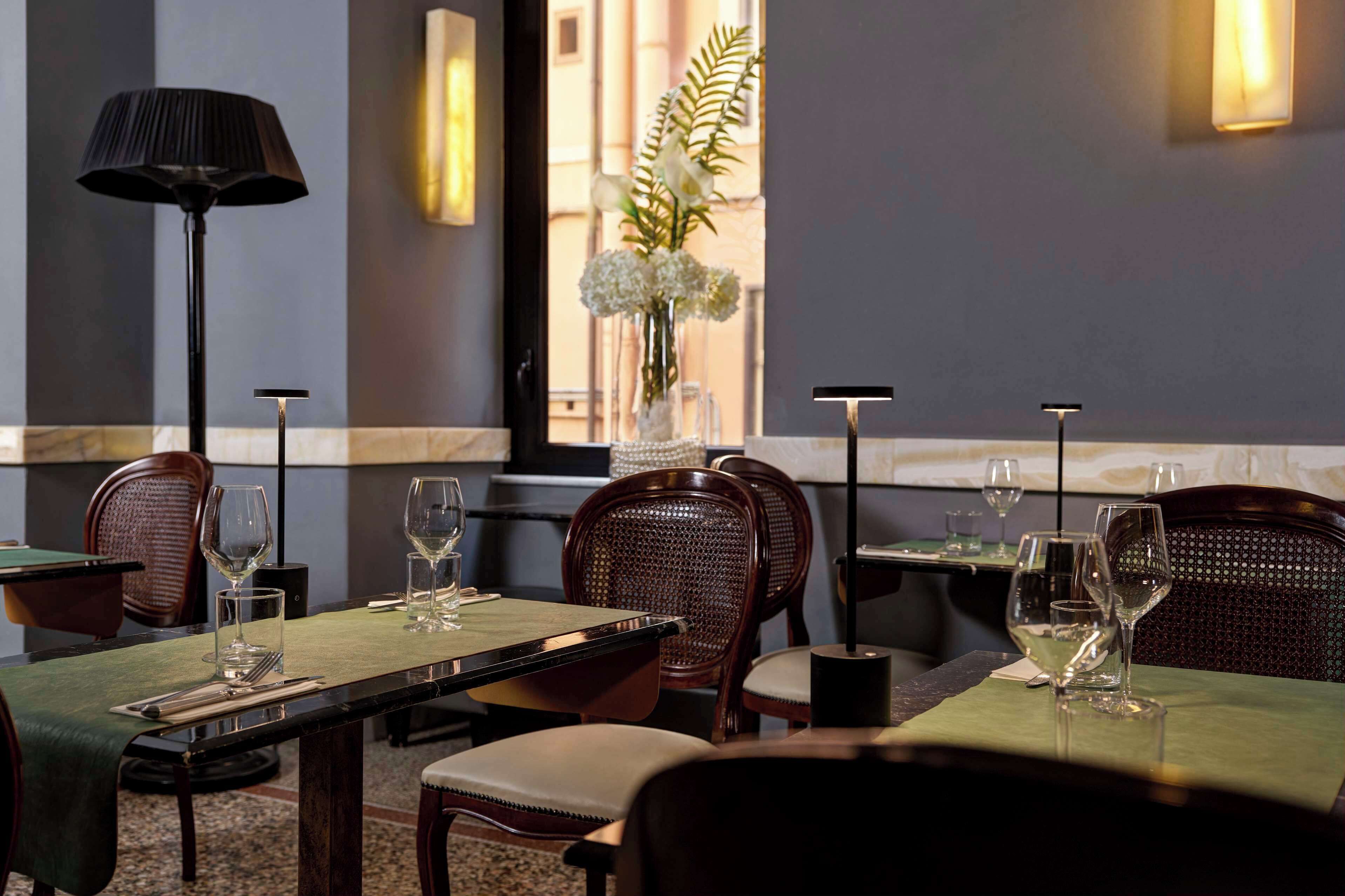 Un restaurante con mesas dispuestas para comer, sillas y un florero con flores.