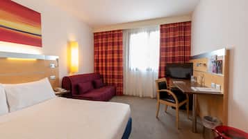 Ein Hotelzimmer mit Bett, Schreibtisch, Stuhl, Fernseher und einem Fenster mit Vorhängen.