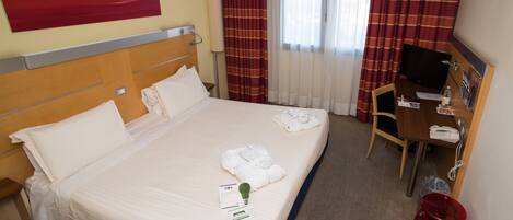 Habitación de hotel con una cama grande, un escritorio con silla, televisión y un dispensador de agua rojo.