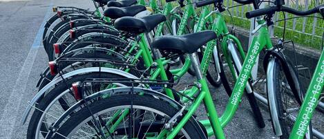 A row of green bicycles parked in a designated area with a metal fence and street lamps in the background.