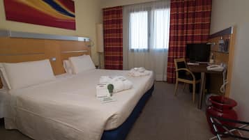 Habitación de hotel con una cama grande, un escritorio con silla, un televisor y un bote de basura rojo.