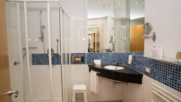 A modern bathroom with a glass-enclosed shower, a black sink, and a mirror above it.