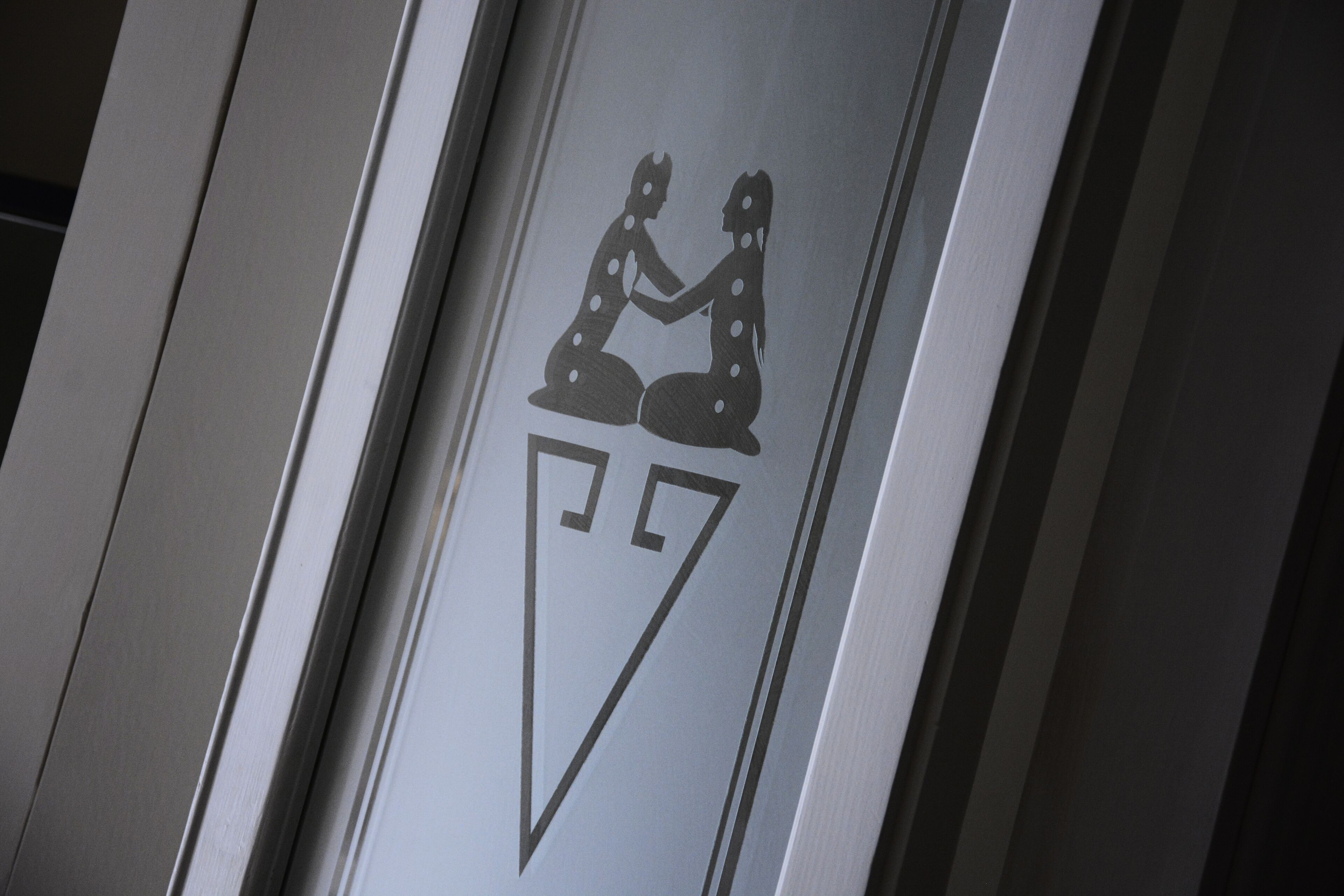 A restroom sign with a silhouette of two people sitting and a triangular symbol.