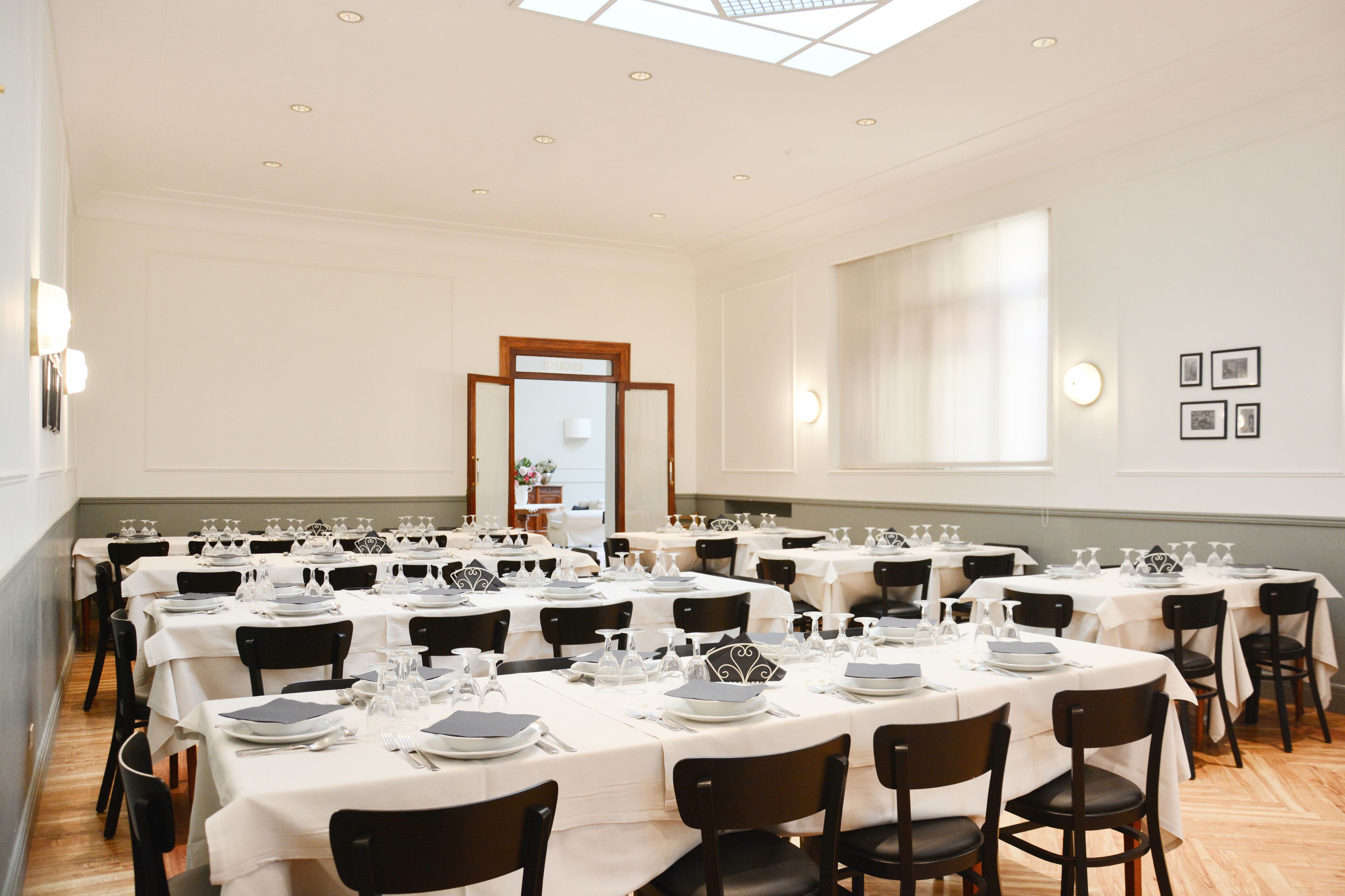 Ein großer Speisesaal mit mehreren runden Tischen, gedeckt für ein festliches Essen, mit weißen Tischdecken und schwarzen Stühlen.