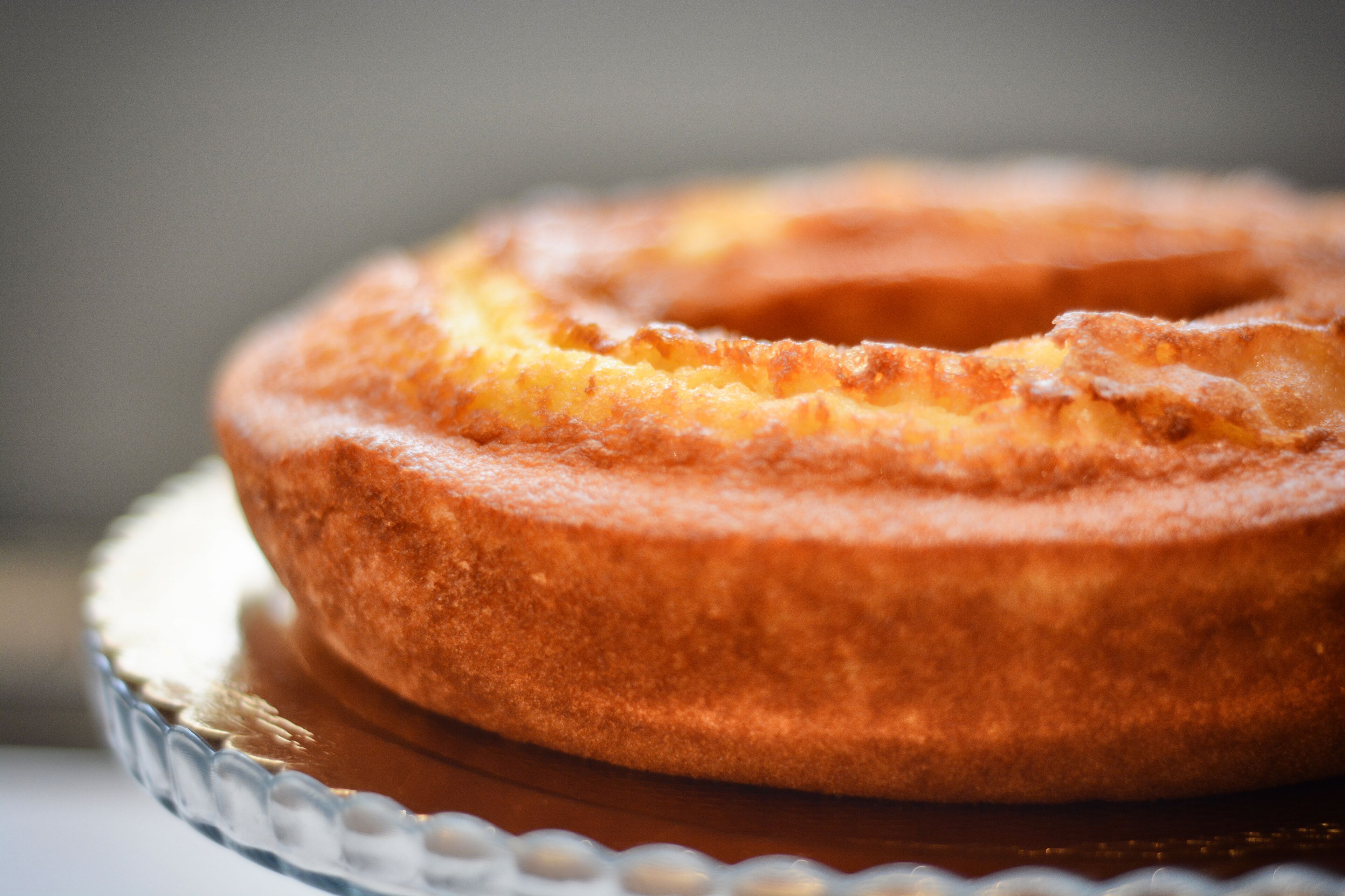 Un pastel redondo con una corteza dorado-café sobre un plato de vidrio transparente.