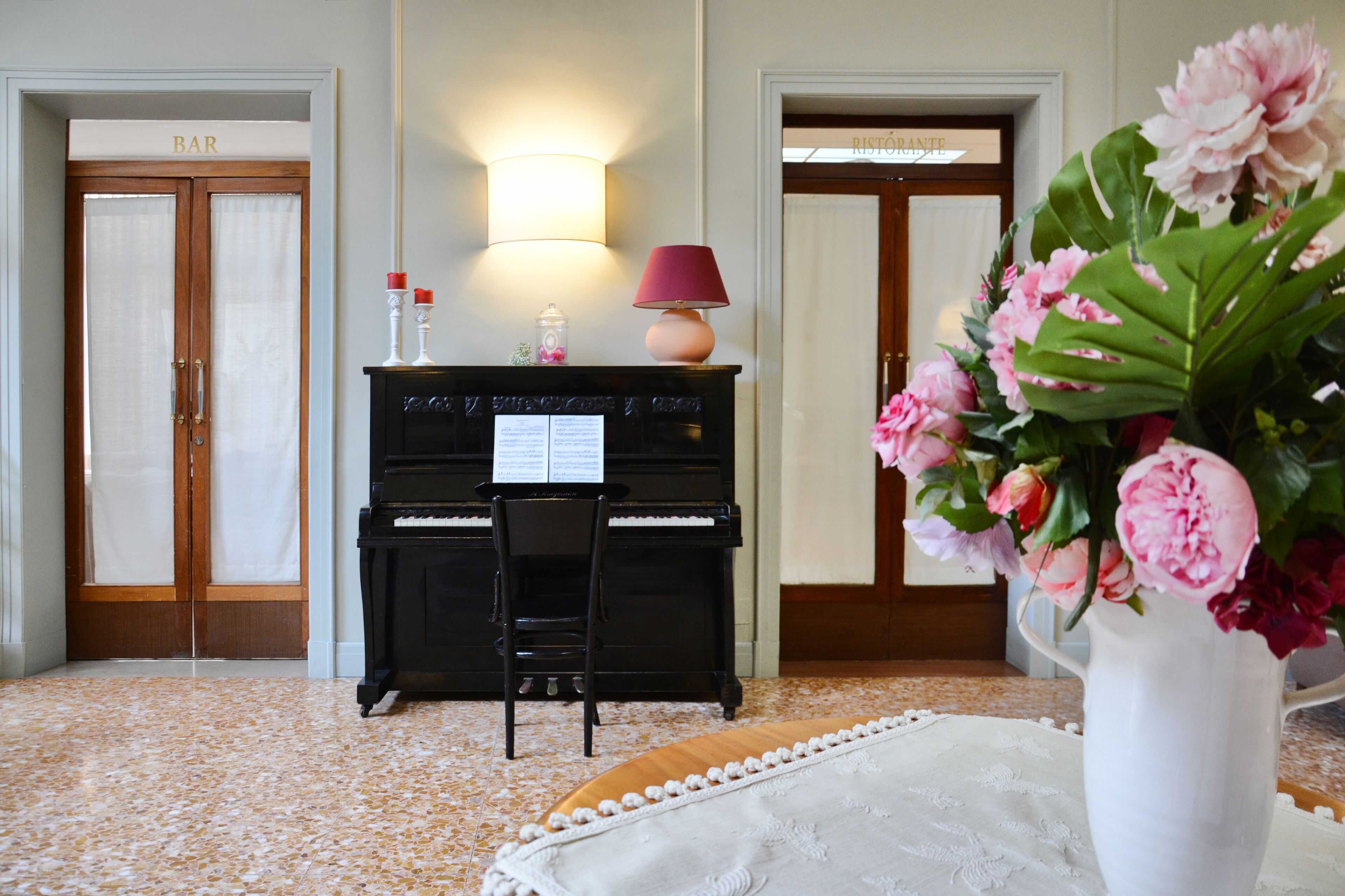 Una stanza con un pianoforte, un vaso di fiori e un cartello che indica un bar.