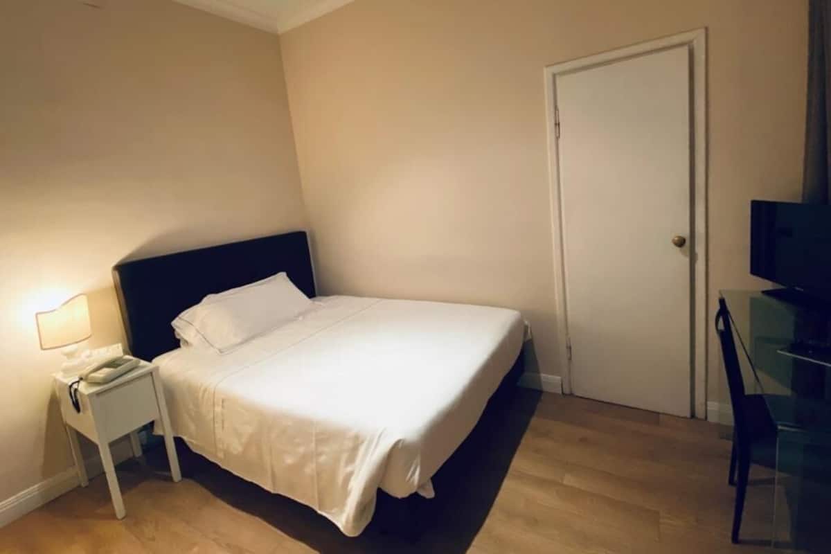 A bedroom with a bed, a nightstand, a desk, and a television.